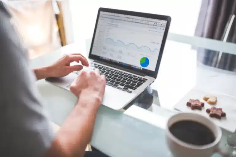 Marketer analyzing Google Ads campaign performance on laptop, reviewing traffic trends and pie chart data at desk with coffee—symbolizing expert ad management and ROI optimization strategies.