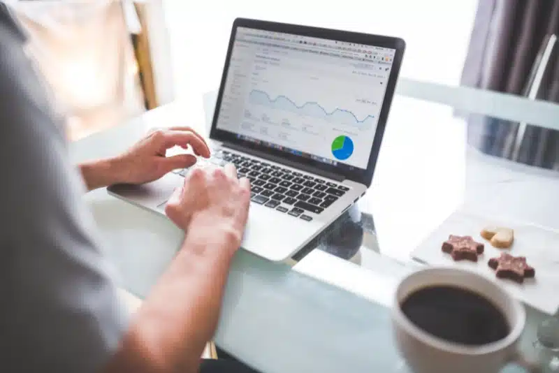 Marketer analyzing Google Ads campaign performance on laptop, reviewing traffic trends and pie chart data at desk with coffee—symbolizing expert ad management and ROI optimization strategies.