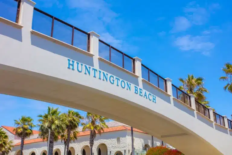 Huntington Beach pedestrian bridge with palm trees and blue sky near the city’s beachfront area.