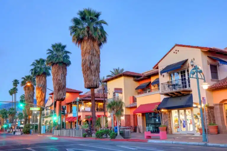 Palm Springs cityscape with palm-lined streets, desert mountains in the background, and clear blue sky.
