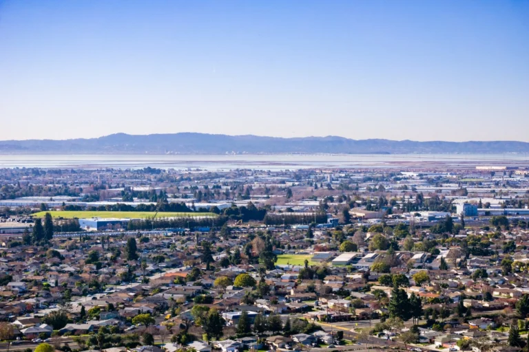 Elevated view of Hayward, California, featuring residential areas, urban development, and distant hills beneath a clear blue sky.