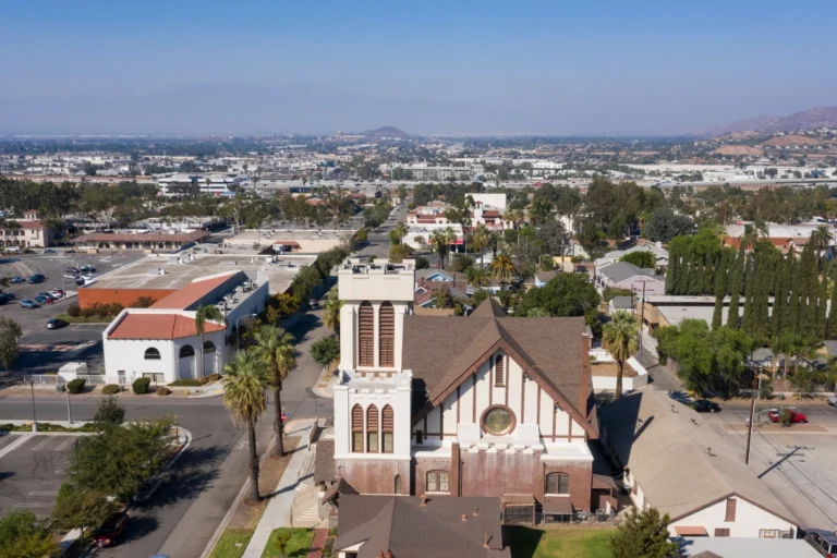 Palm-lined boulevard in Corona, California, with landscaped streets, residential buildings, and mountain views in the background.