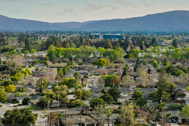 Aerial view of Sunnyvale, CA featuring tree-lined neighborhoods, modern office buildings, and rolling hills under a clear daytime sky.