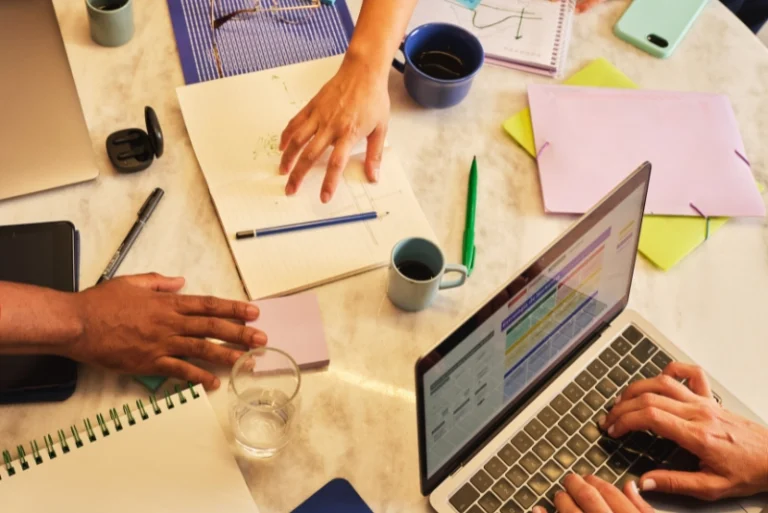 A group of individuals collaborating at a table, each focused on their laptops, engaged in a work session.